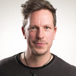 Mann mit selbstbewusstem Ausdruck, freundliches Lächeln, kurze braune Haare.