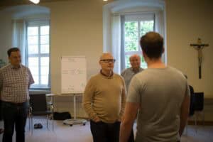 Männer im Gespräch während eines Workshops oder Meetings in einem hellen Raum.