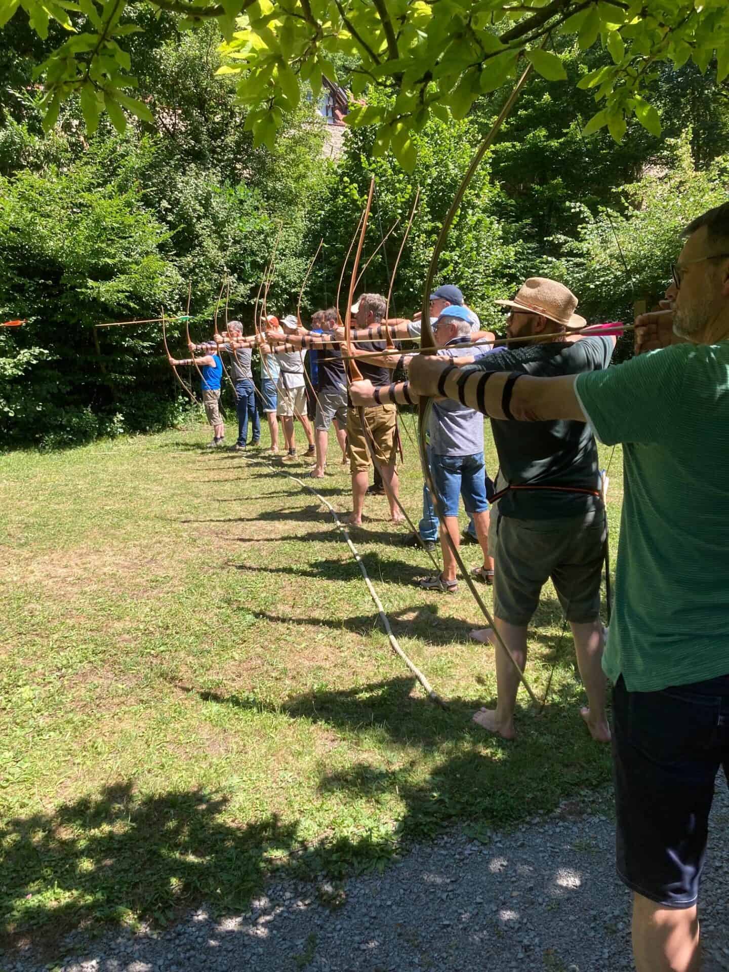 Männer beim Bogenschießen im Freien, in einer grünen Parklandschaft, bei einem Outdoor-Workshop.