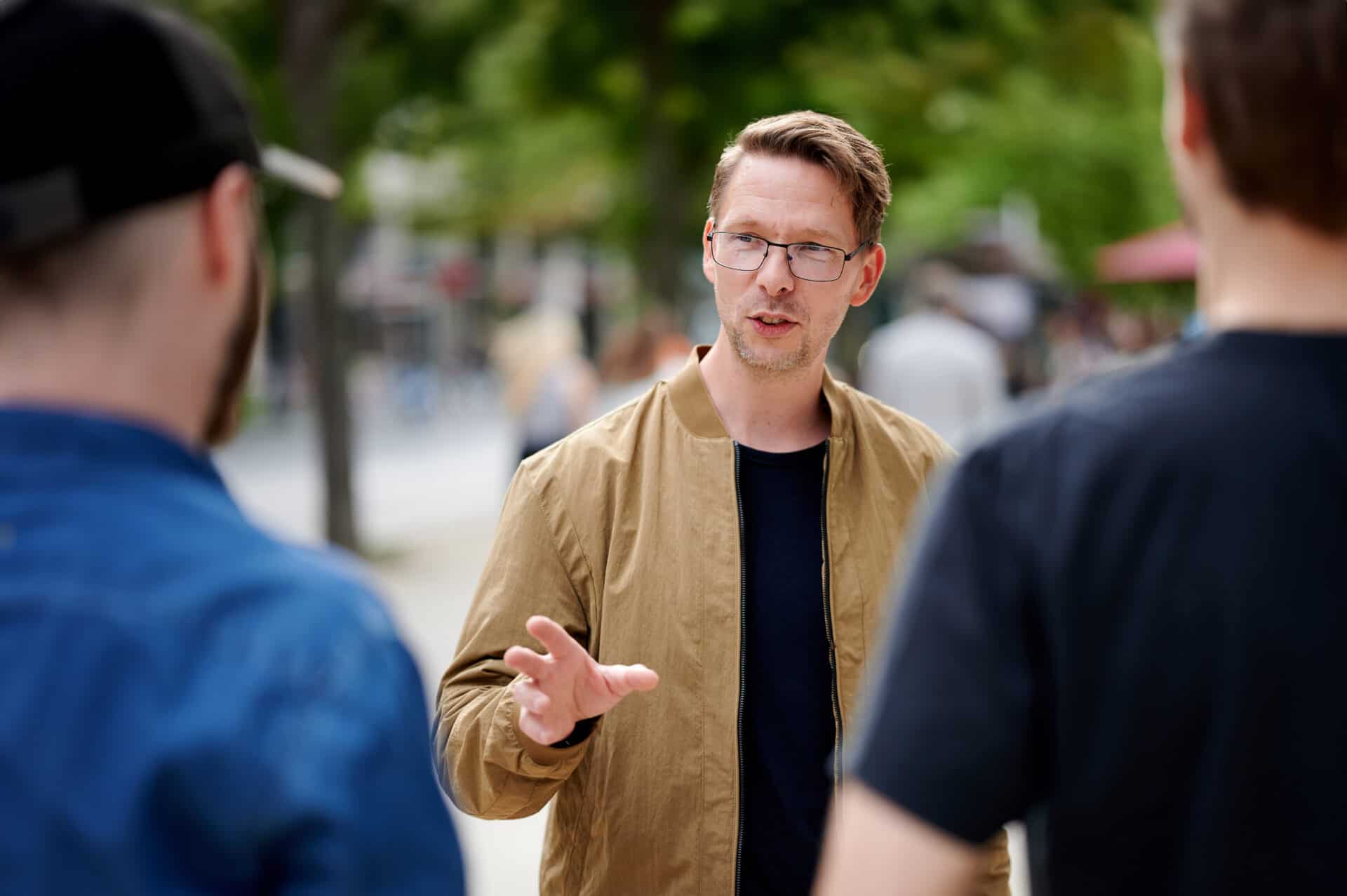 Männer im Gespräch im Park, Fokus auf einen Mann, der spricht, mit zwei Zuhörern im Vordergrund.
